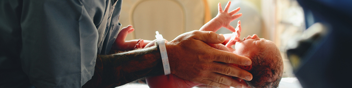 A newborn baby being held by a healthcare professional, representing compassionate care at birth.